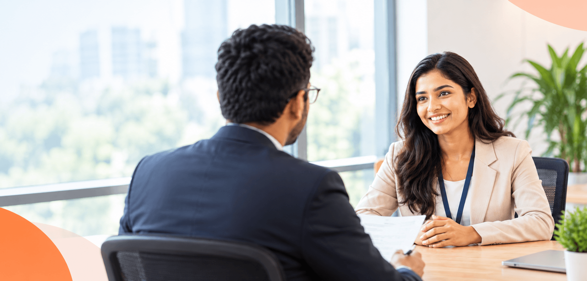 Job interview questions and answers in English for freshers, featuring a young woman speaking with an interviewer in a modern office.